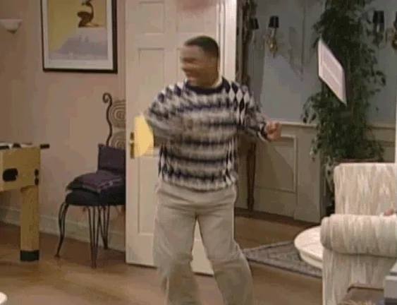 a black man in a sweater does a backflip and jumps in excitement with papers falling around him